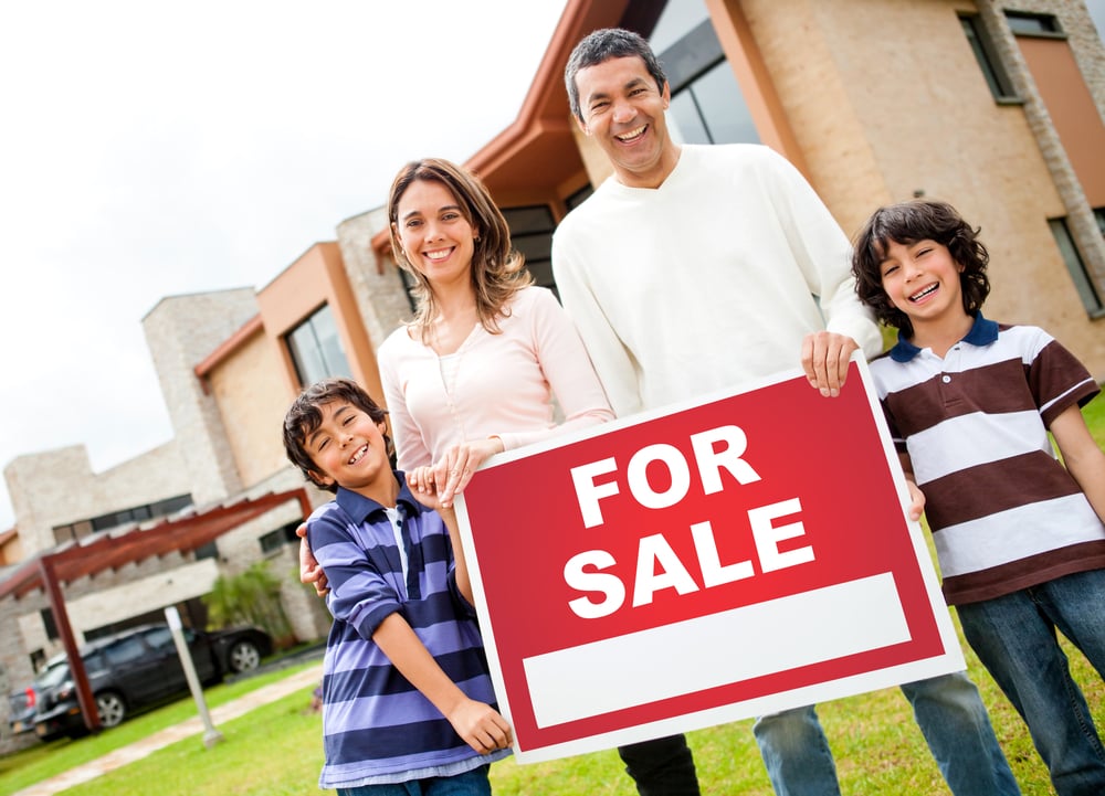 Happy family holding a 'for sale' sign, representing the importance of property marketing to attract buyers.