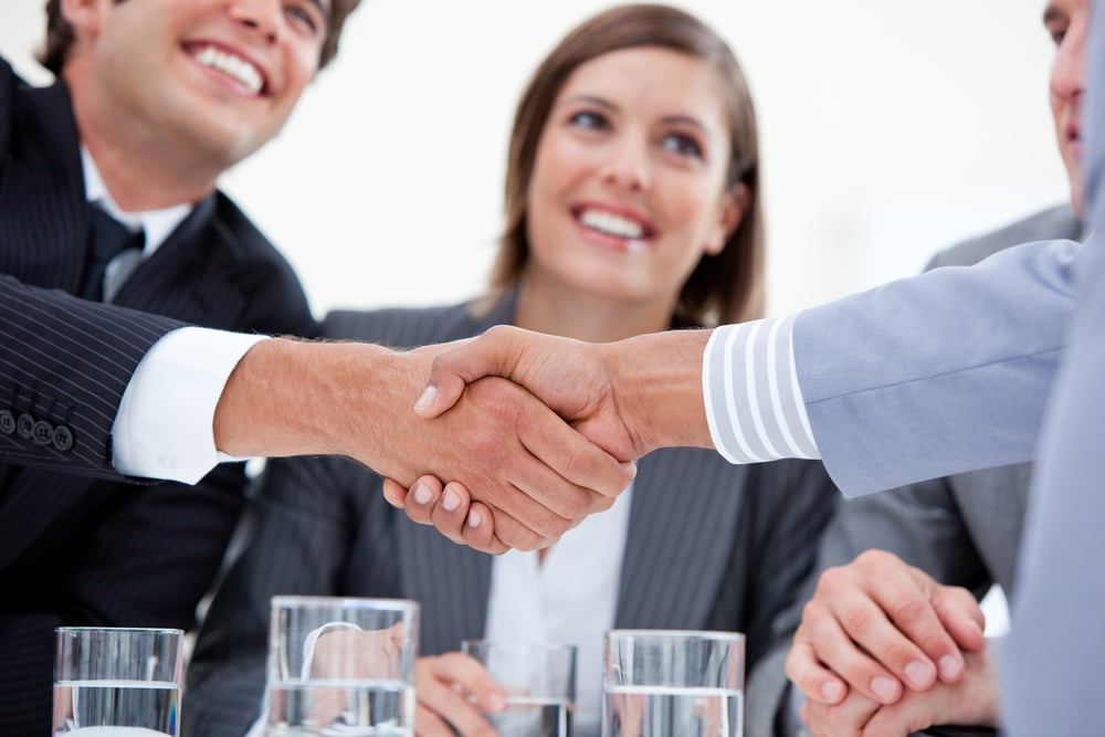 Two real estate agents shaking hands after negotiating agent commission for a property sale.